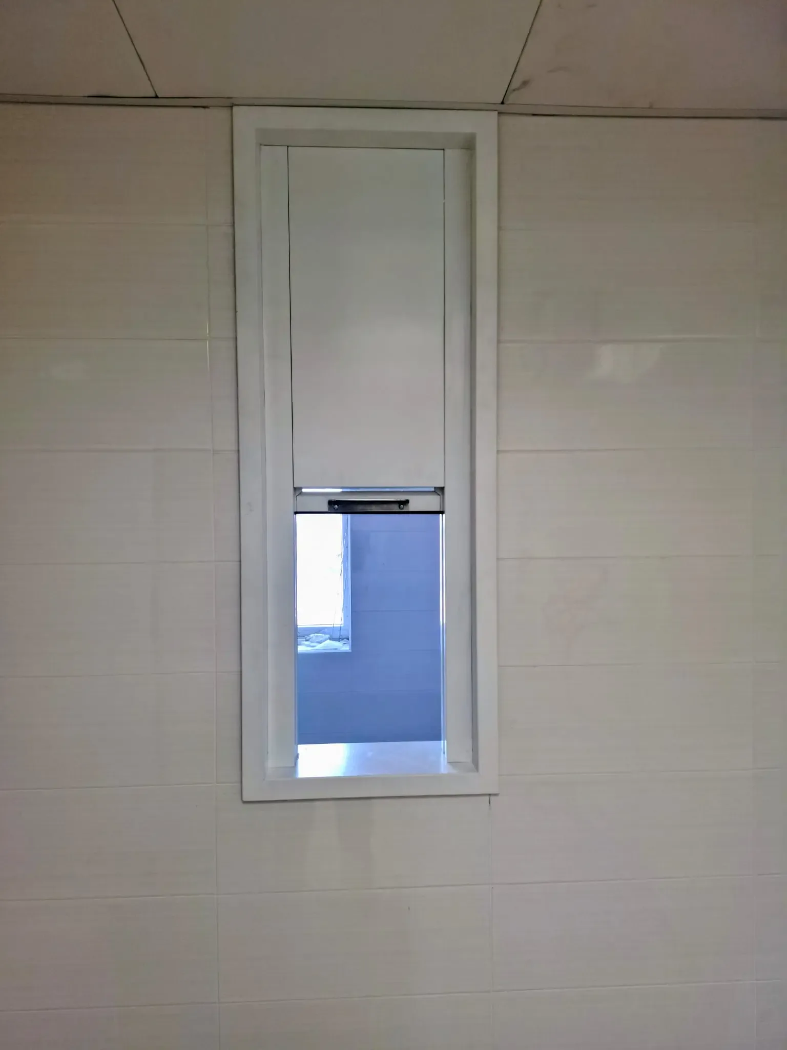 A narrow protective lead window set into a wall clad in ceramic tiles