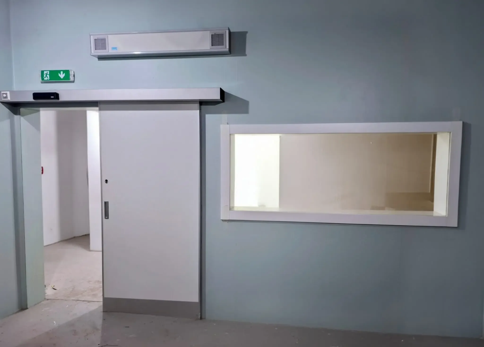 Large-format protective lead glass in a white frame, beside a powered automatic door