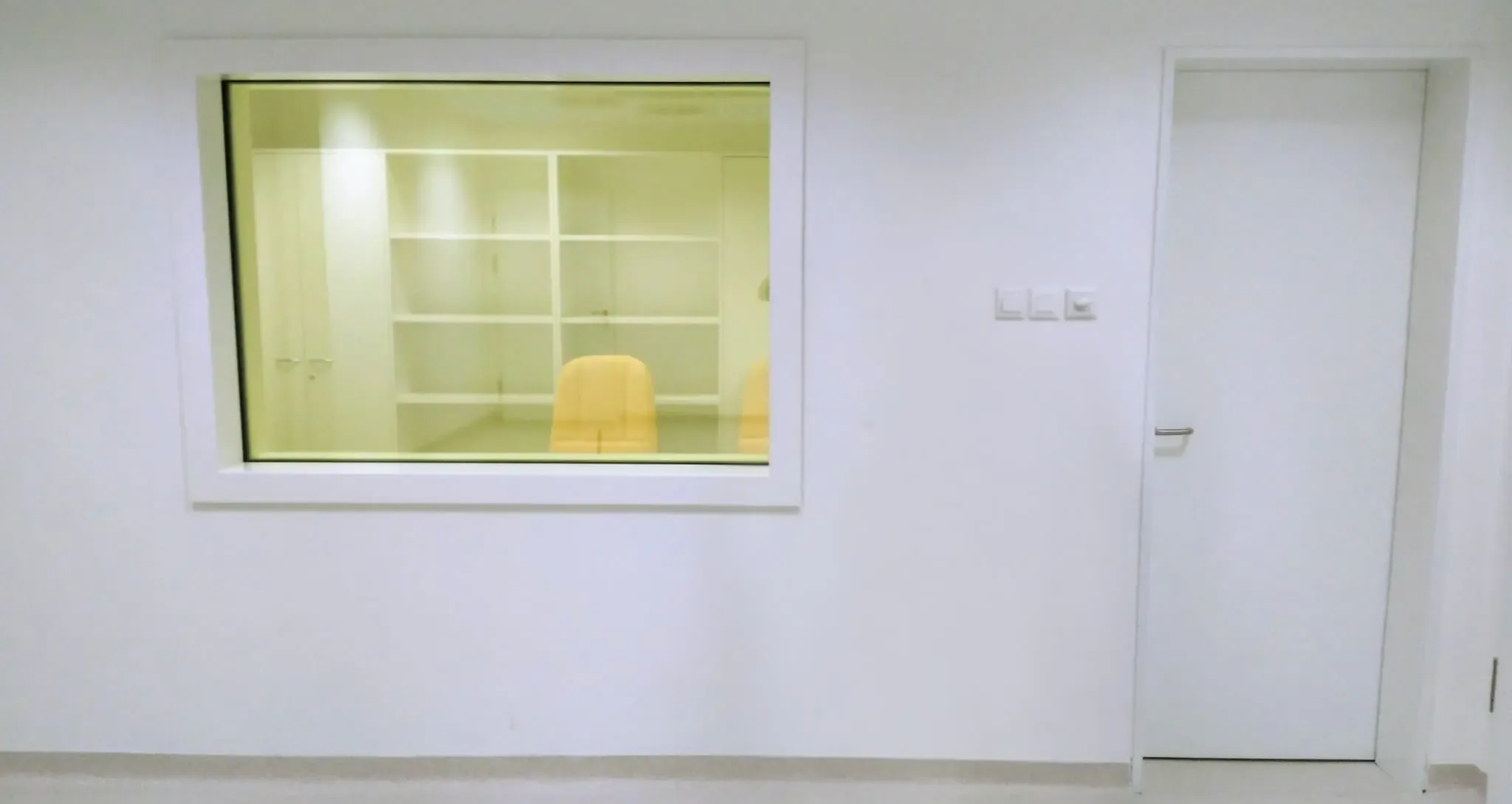 Protective lead glass in a white frame in a partition wall, beside a door