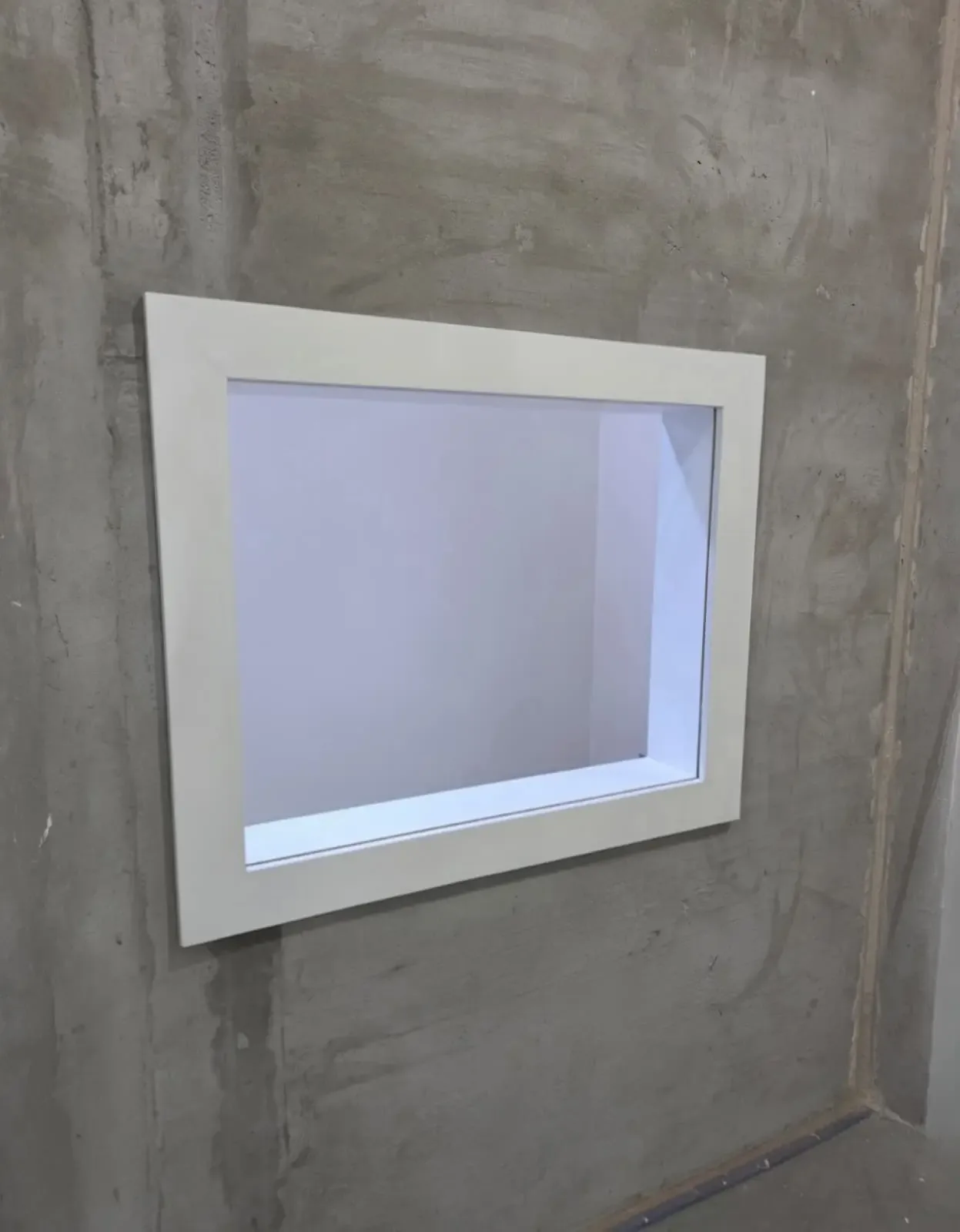 Protective lead glass in a white frame set into a concrete wall during construction