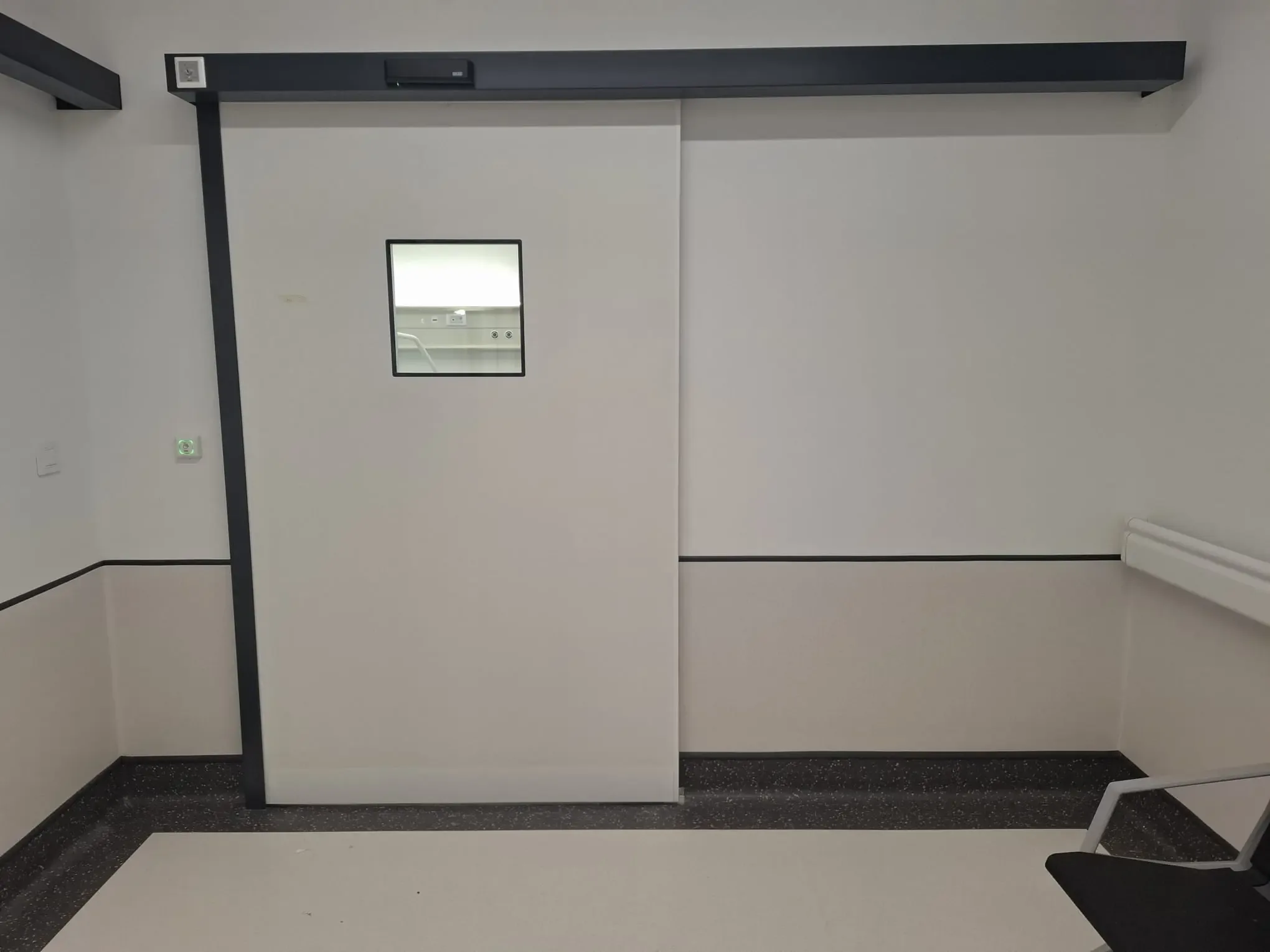 A single-leaf automatic sliding door with a small vision panel and a drive in a dark housing