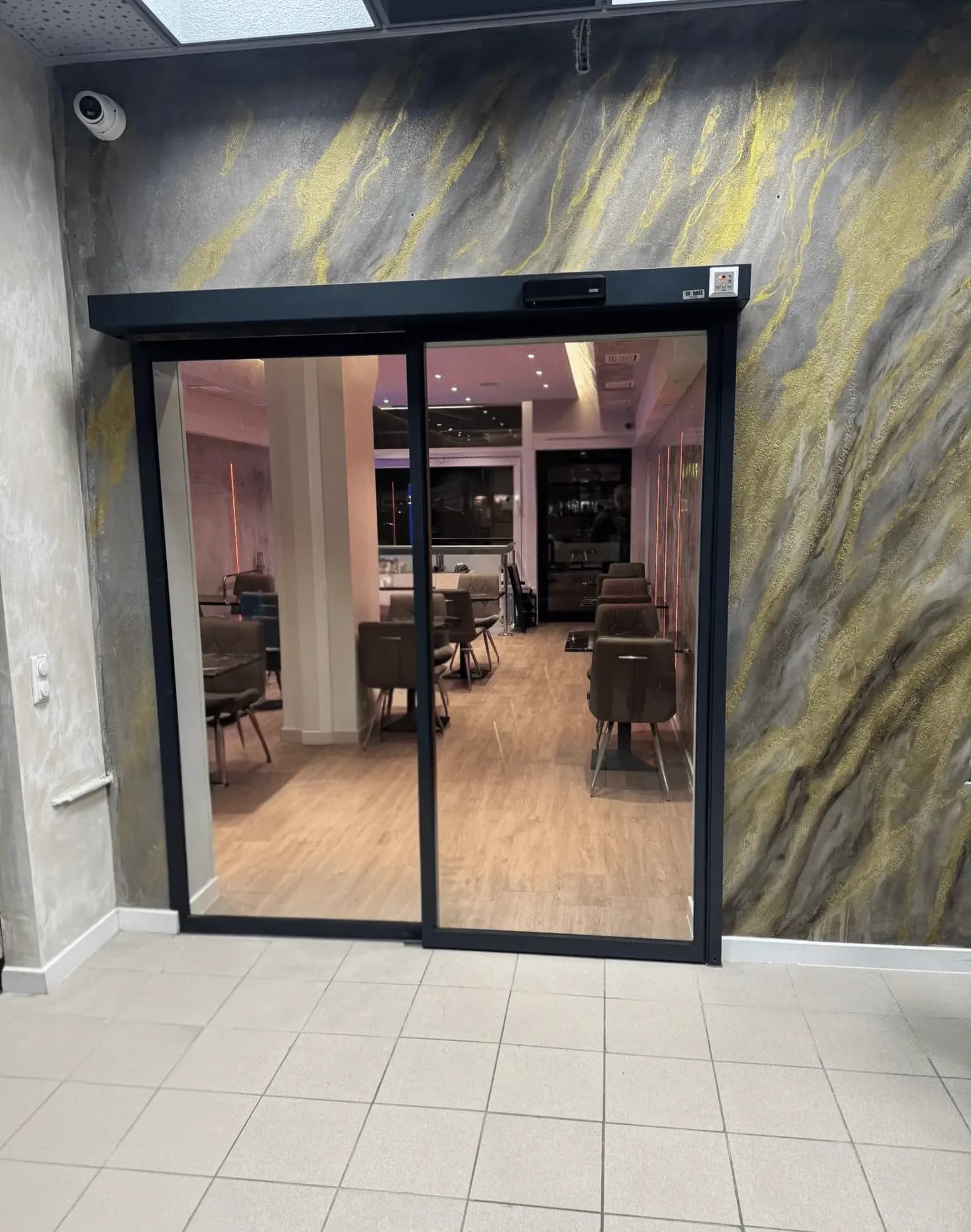 Glazed automatic sliding doors with a black frame set in a decorative stone wall, at the entrance to a hospitality venue