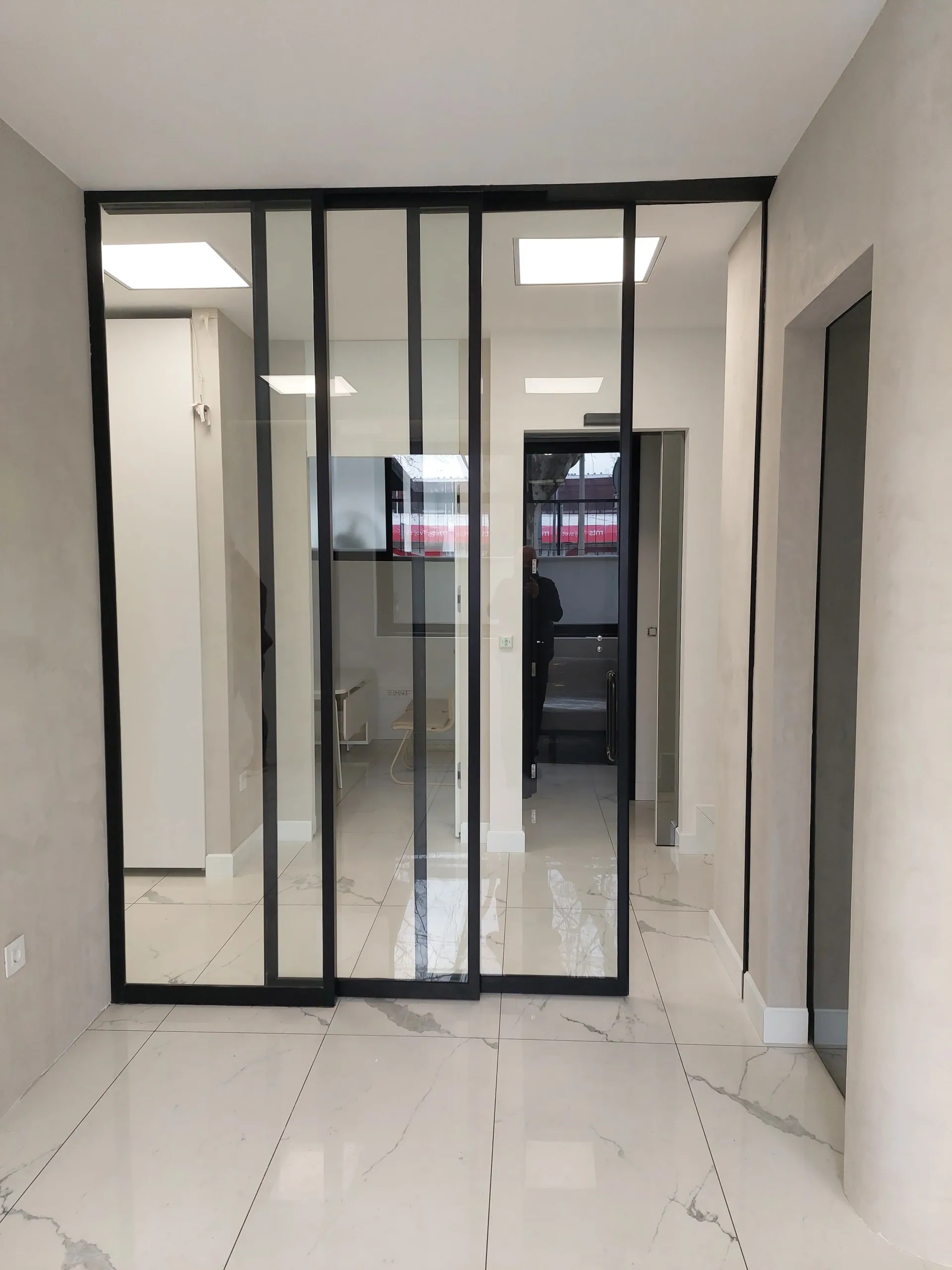 Glazed automatic sliding doors with a black frame used as a partition in an office space with a marble floor