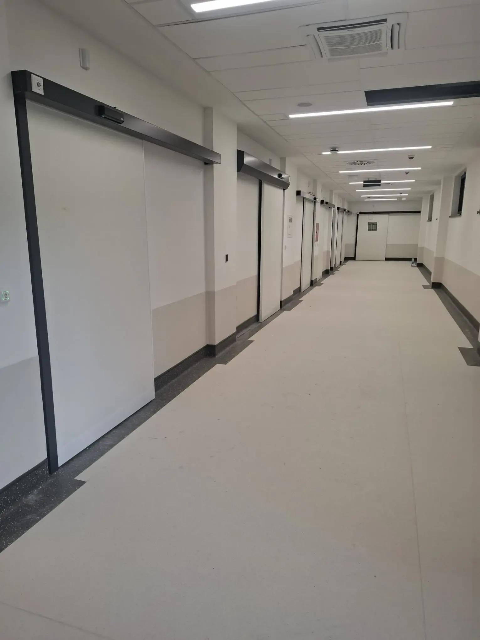 A row of automatic sliding doors with drives in dark housings along a hospital corridor