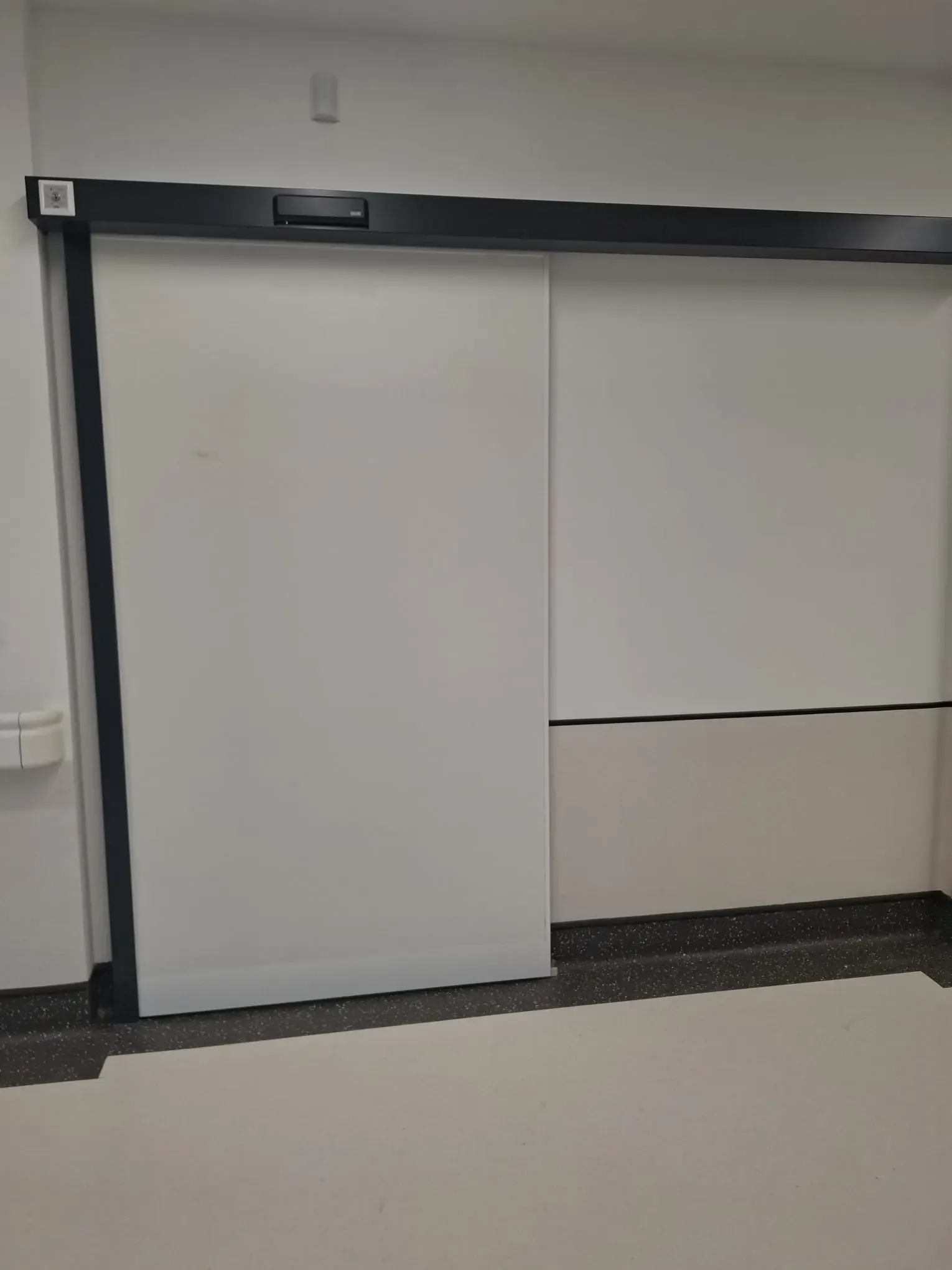 An automatic sliding door with a solid leaf and a drive in a dark housing above the transom
