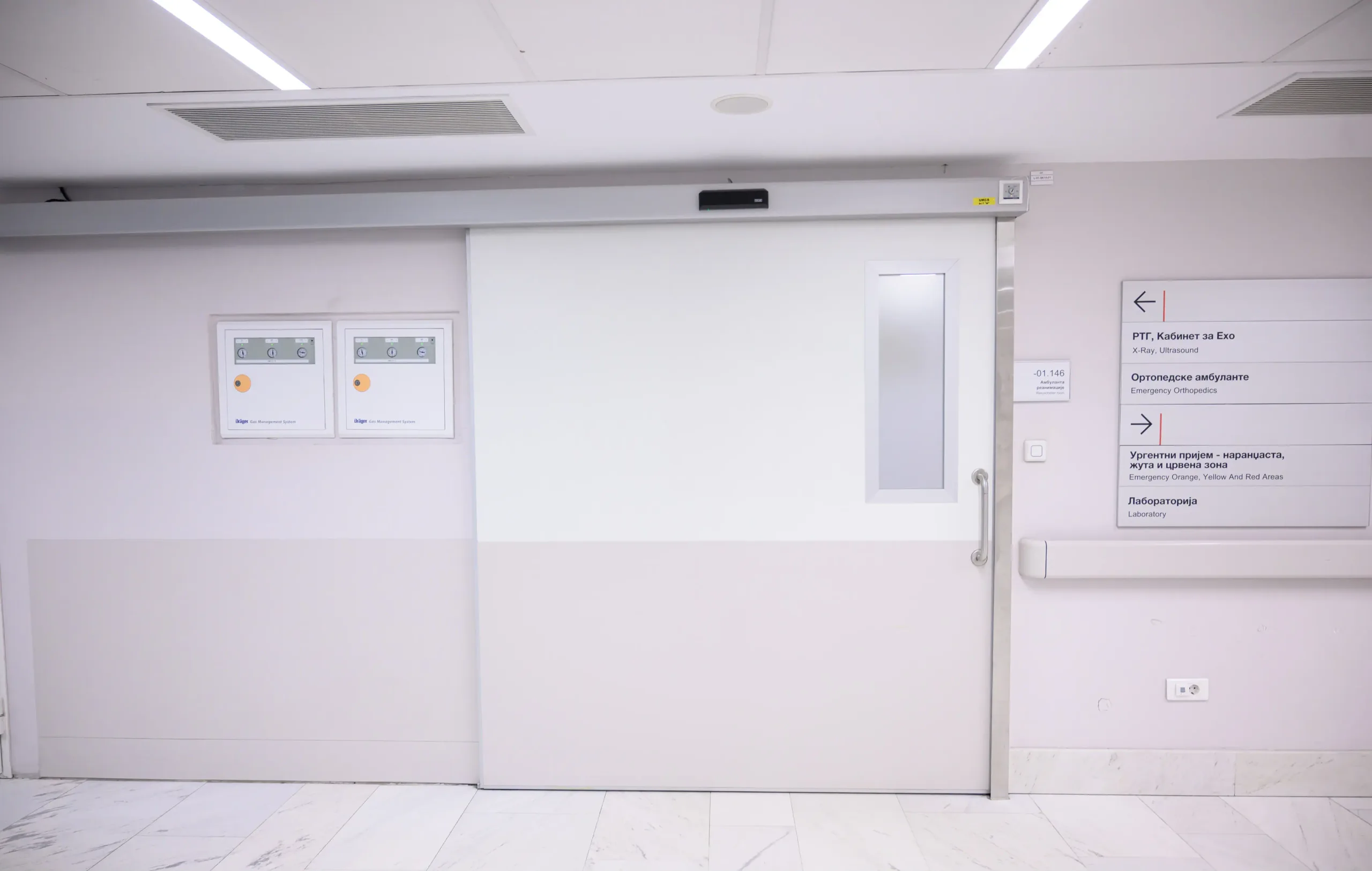 An automatic sliding door with a narrow vision panel in a healthcare building, beside a signage board