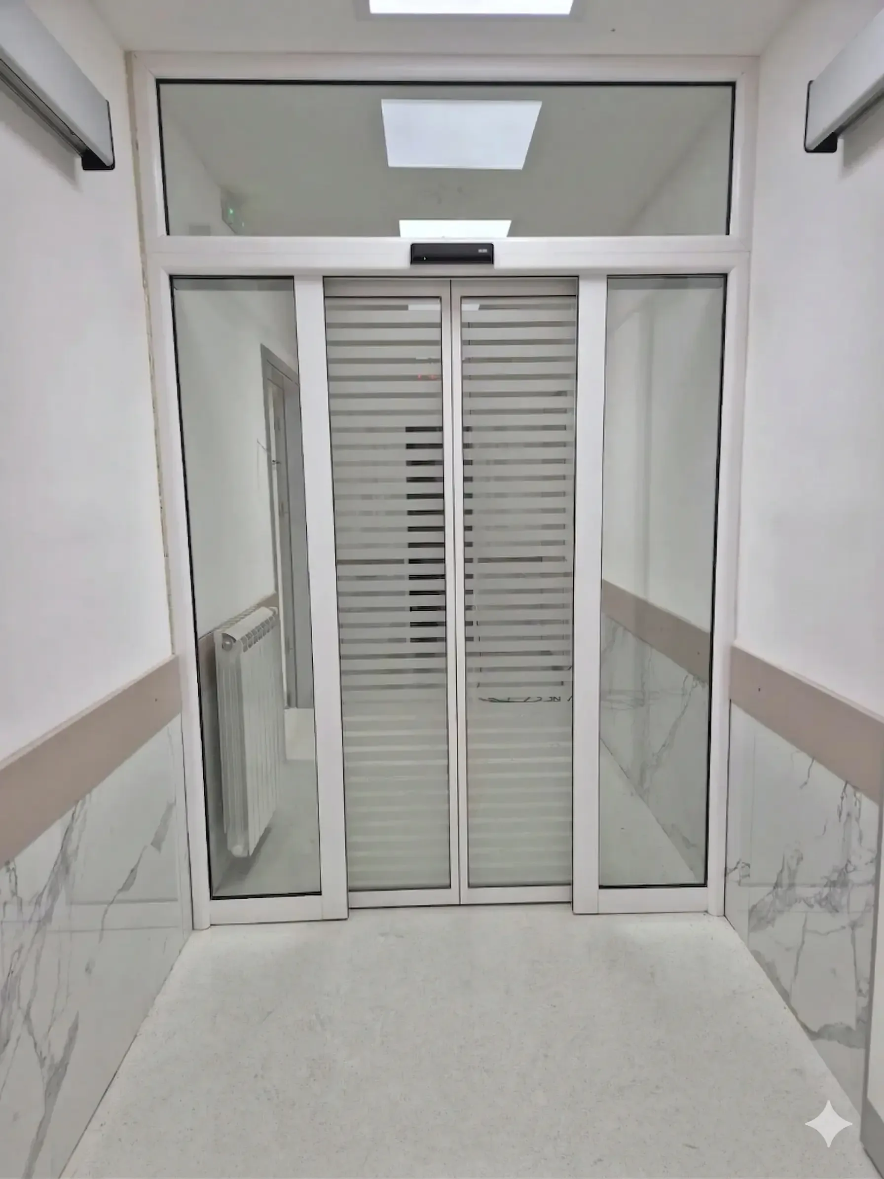 Glazed automatic sliding doors with an aluminium frame and the drive in the transom, in a corridor with a protective wall rail