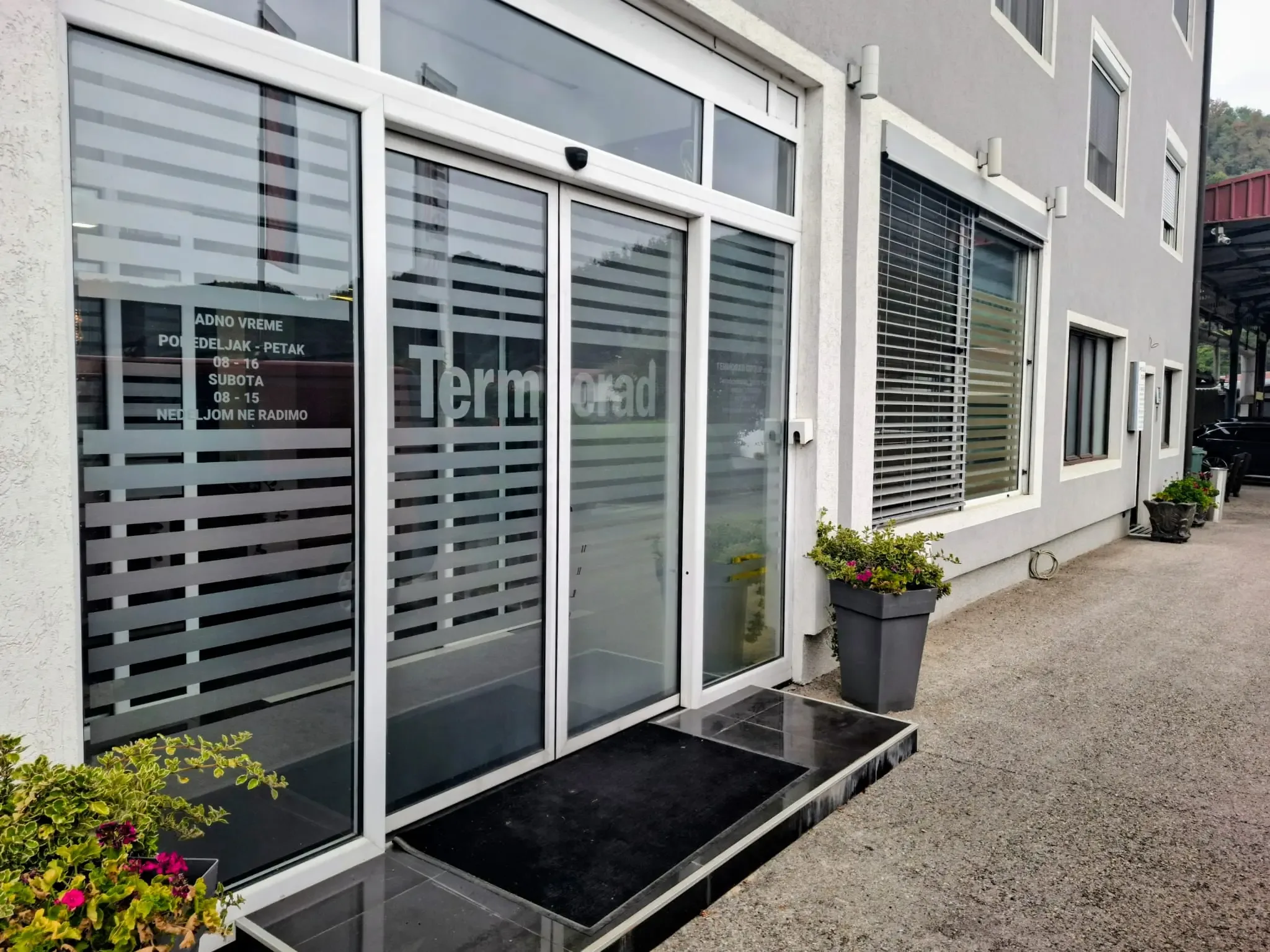 Glazed automatic sliding doors with a white frame and decals on the leaf, at the street entrance to a commercial unit