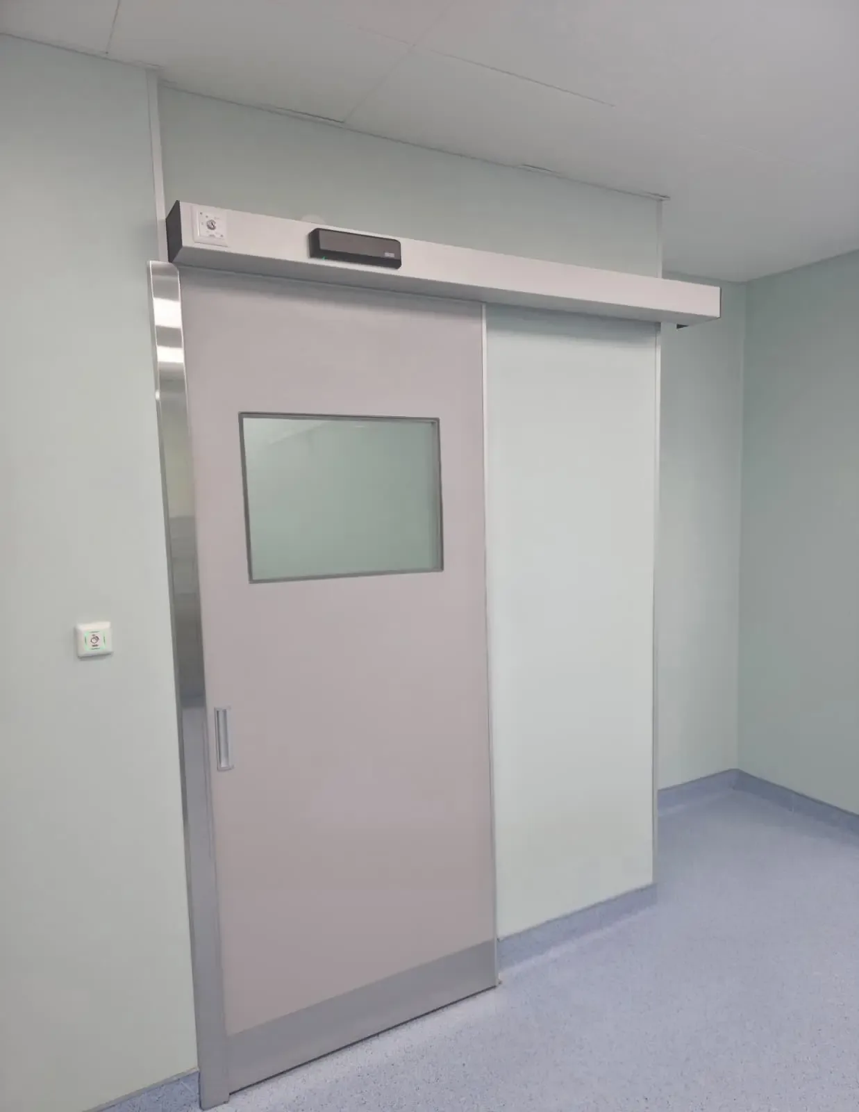 A single-leaf automatic sliding door with a frosted vision panel and the drive above the frame, in a healthcare building