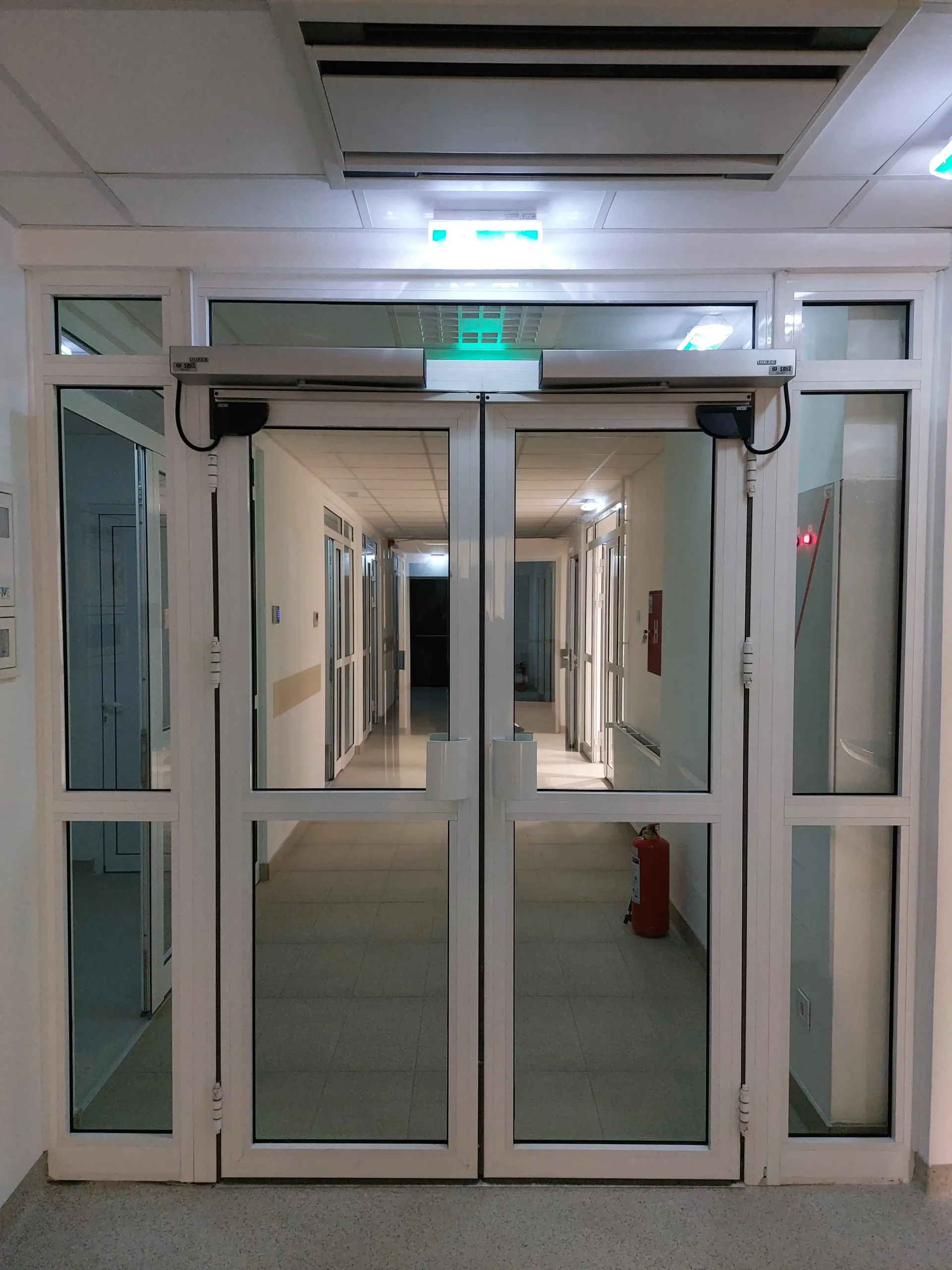 Double-leaf automatic swing doors with glazed infills and drives on the transom
