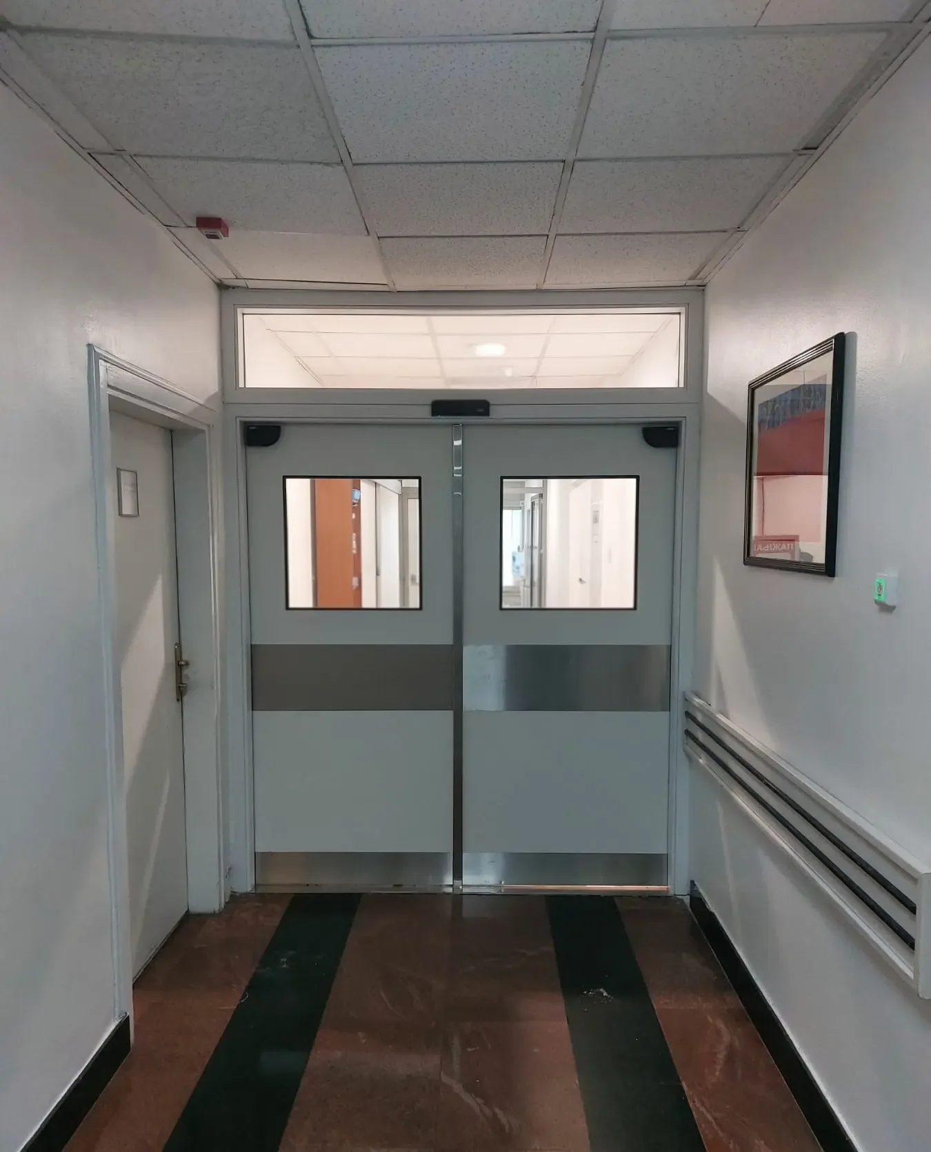 Double-leaf automatic swing doors with vision panels and stainless steel kick plates, at the end of a corridor