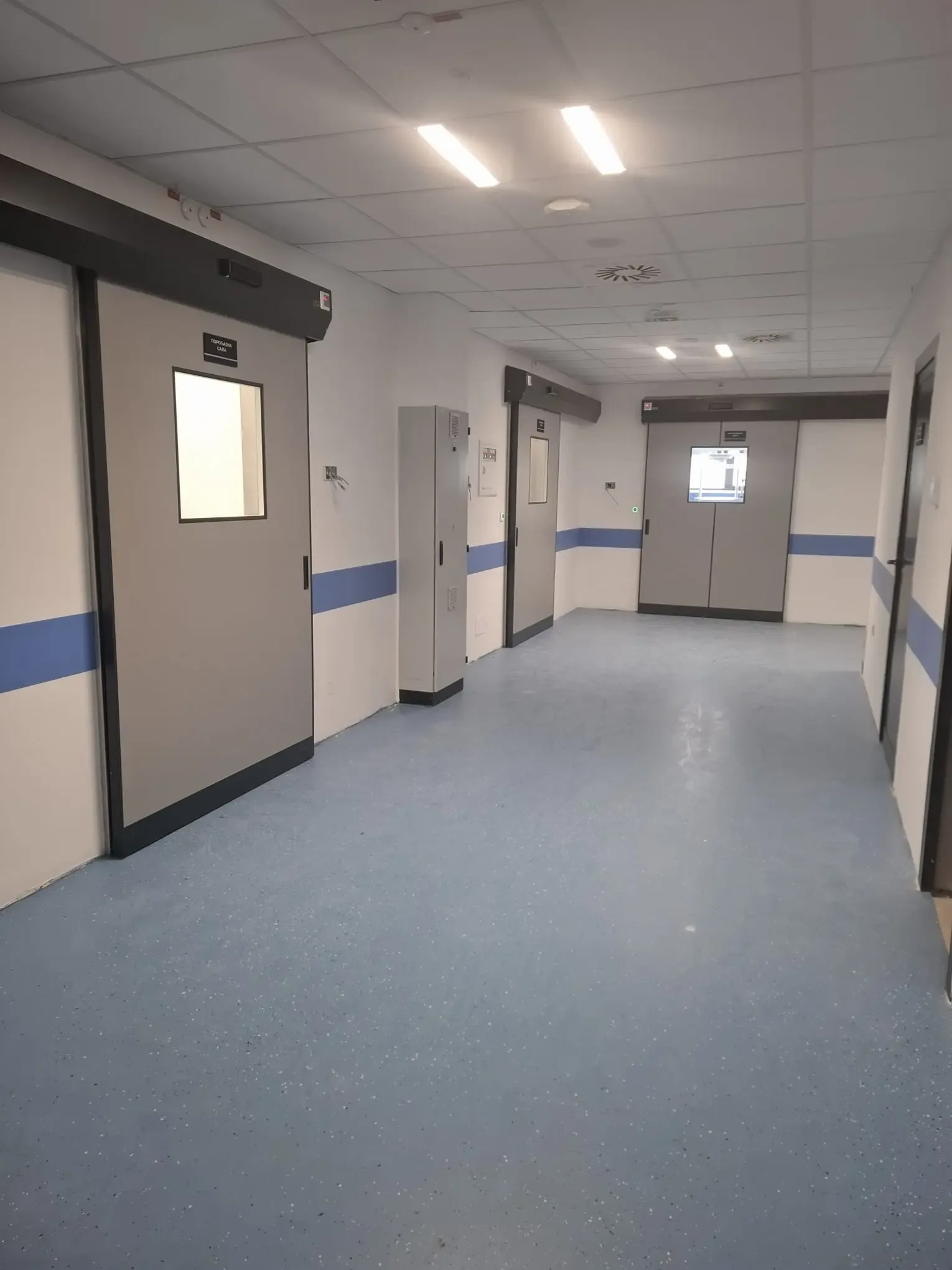 A corridor with hermetic sliding doors to operating theatres and a blue protective wall rail