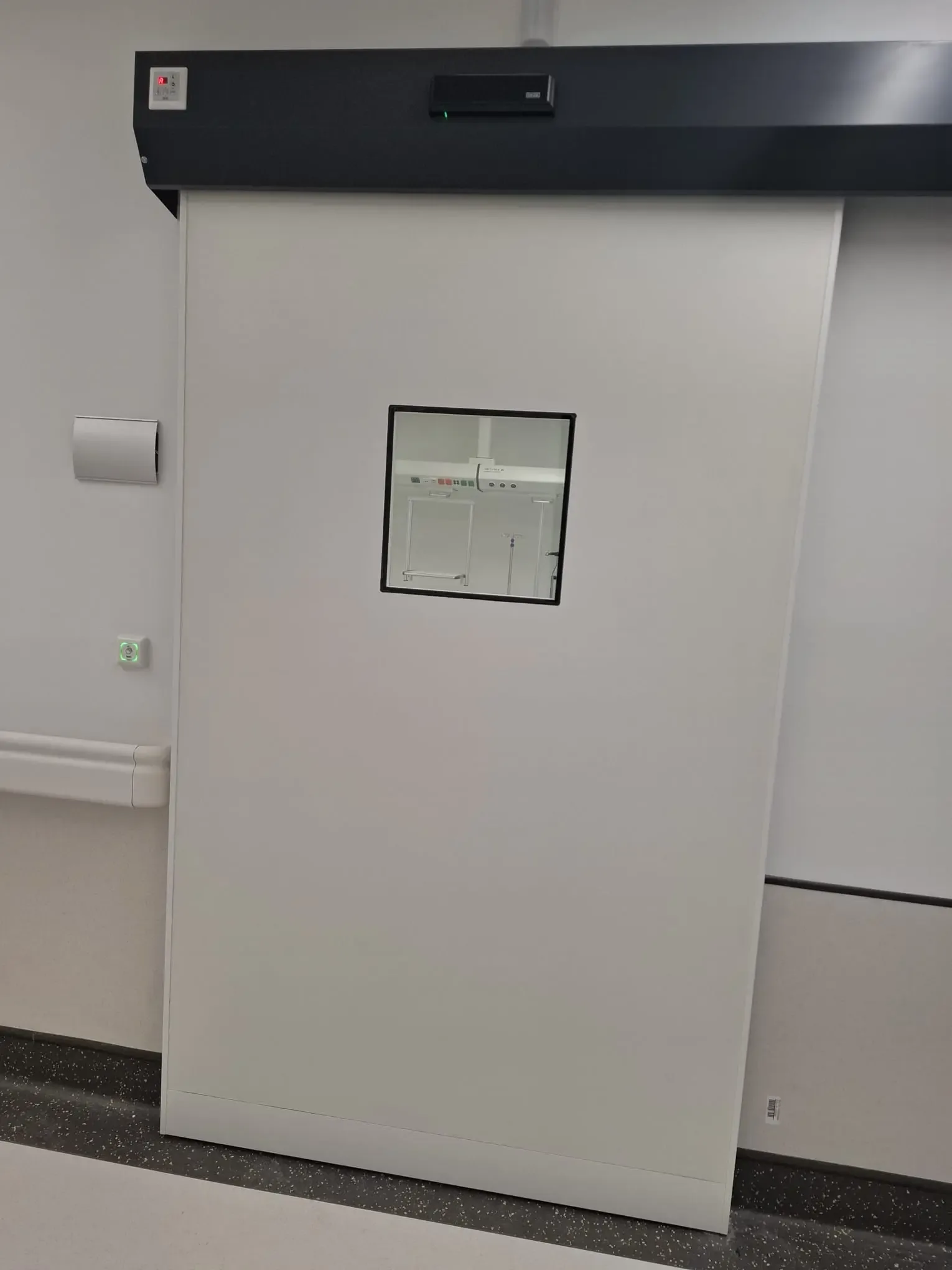 A hermetic sliding door with a white leaf, a vision panel and the drive in a black housing