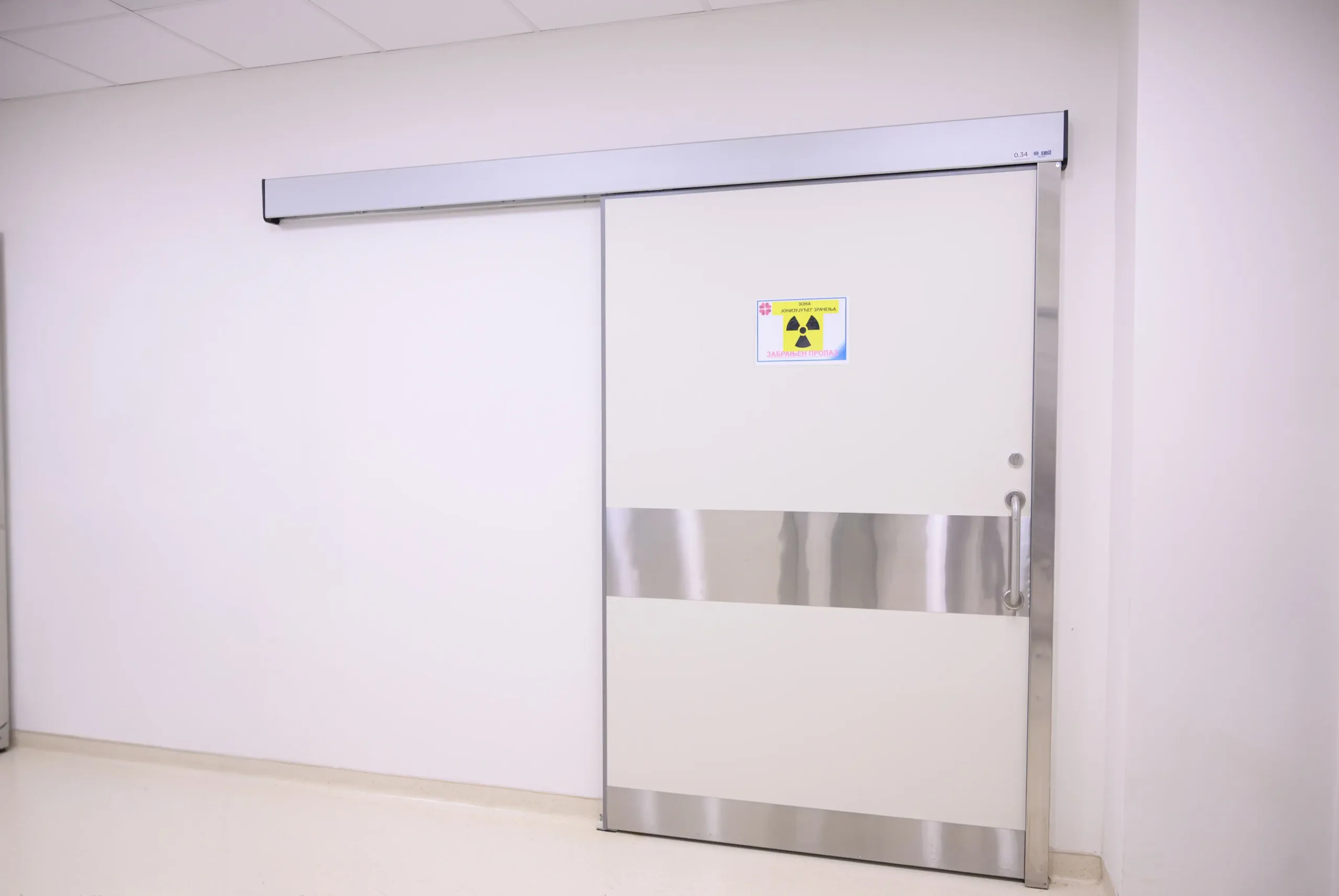 A lead-lined sliding door with an ionising radiation sign, a stainless steel kick plate and a track above the opening