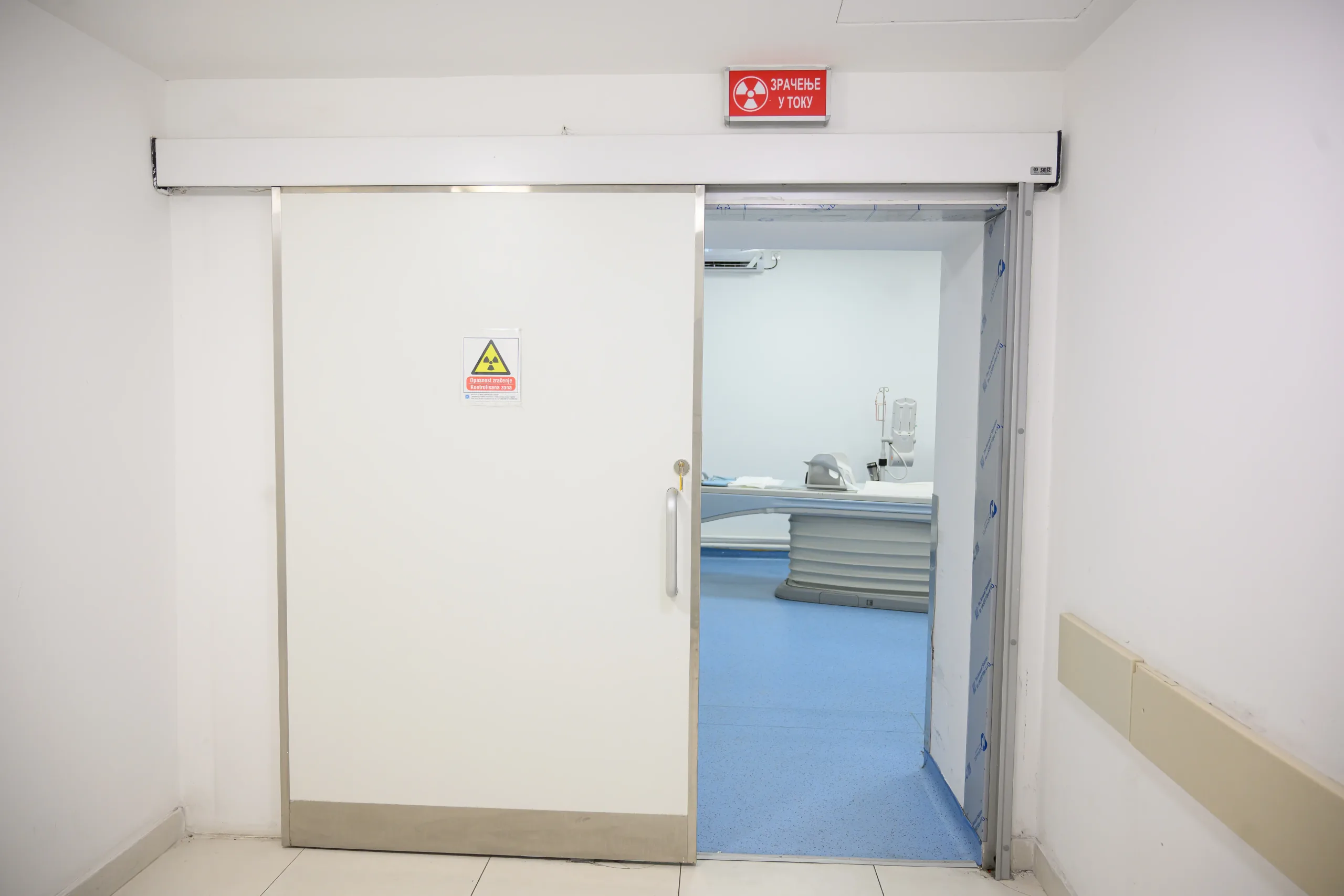 An open lead-lined sliding door to an X-ray room, with an ionising radiation sign and a red illuminated panel