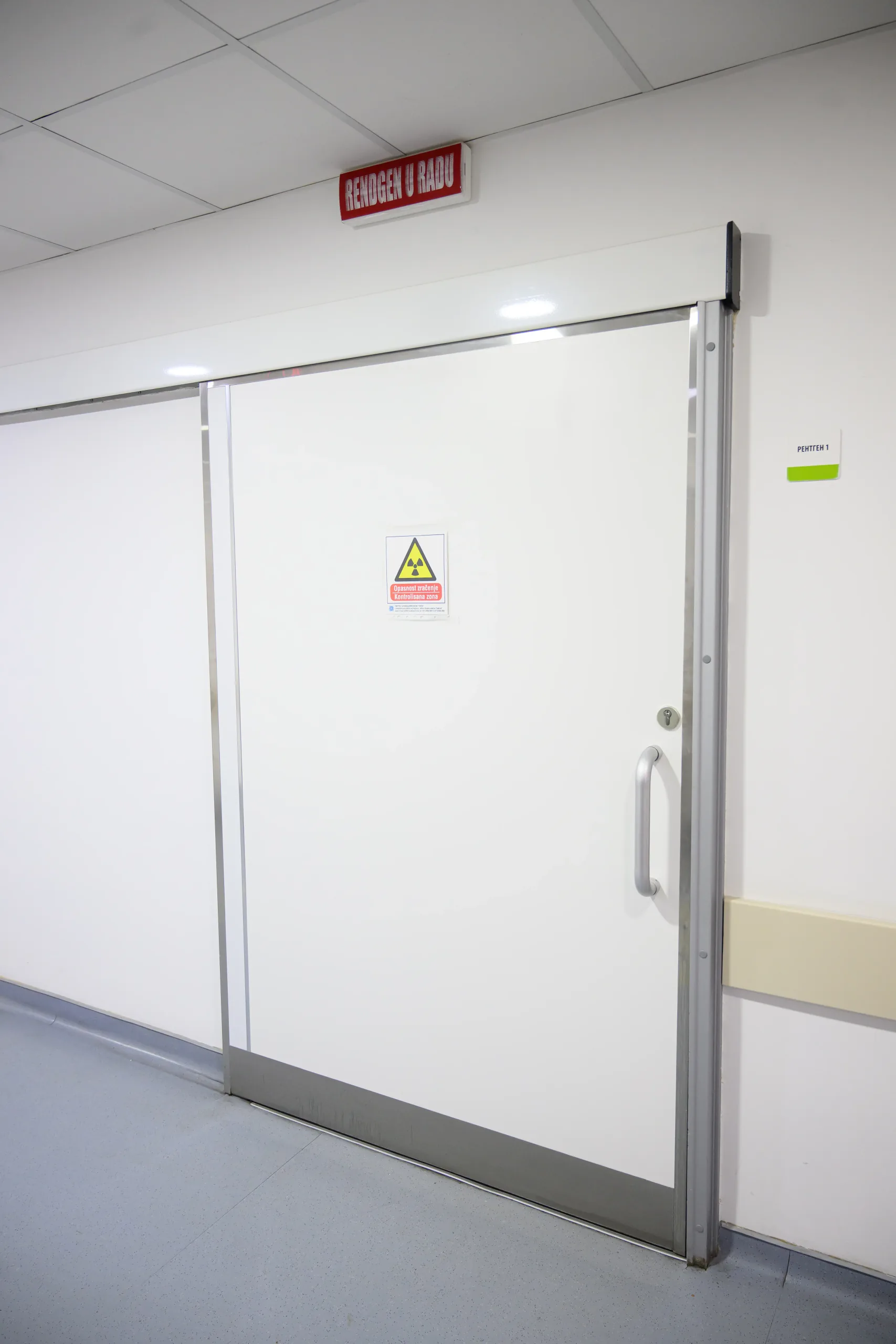 A lead-lined sliding door with an ionising radiation sign, stainless steel leaf edges and a long pull handle