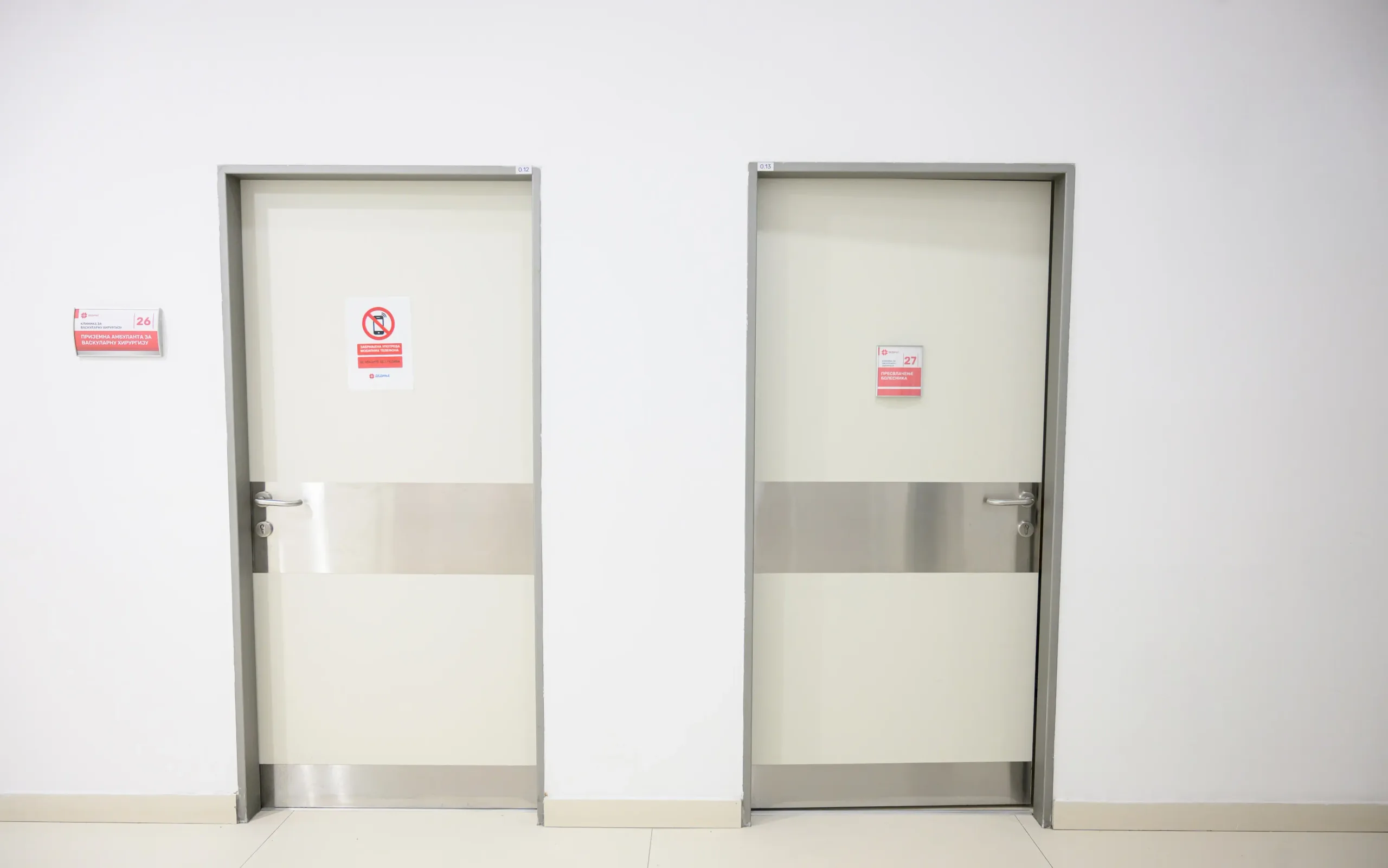 Two single-leaf white doors with stainless steel kick plates and signage on the leaf