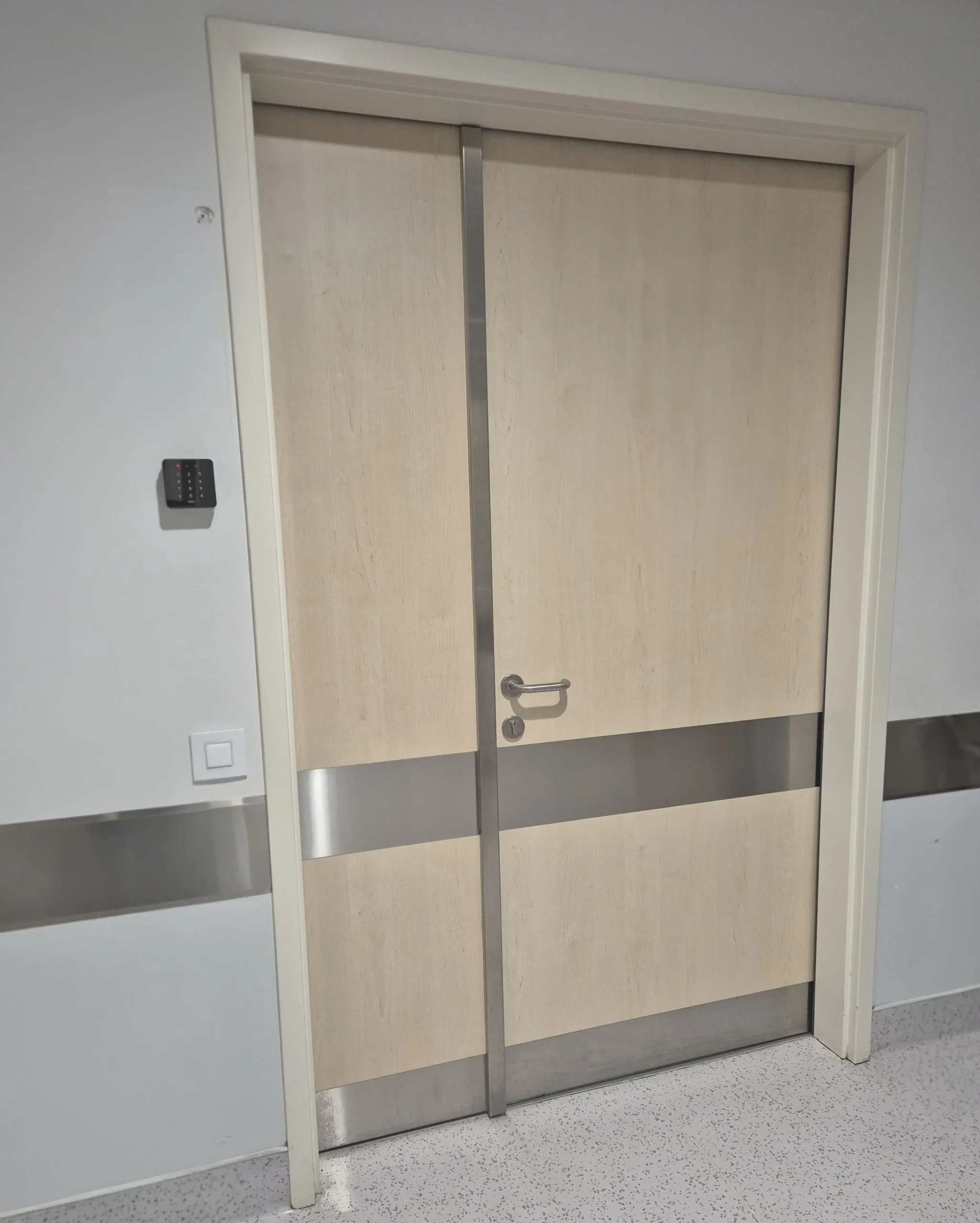 Double-leaf swing doors in a light timber finish with a stainless steel protection strip across both leaves