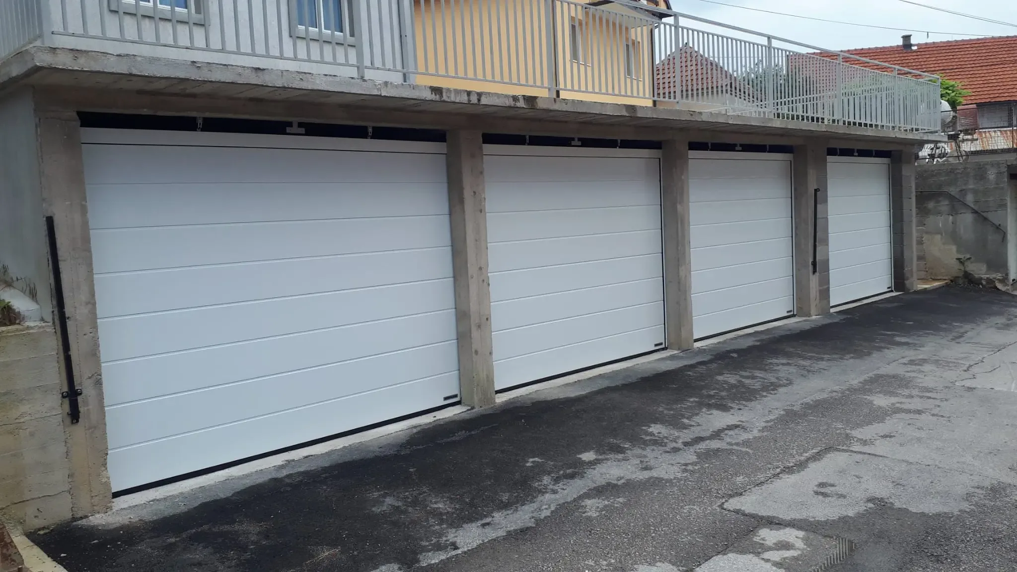 A row of four white sectional garage doors on the ground floor of a residential building