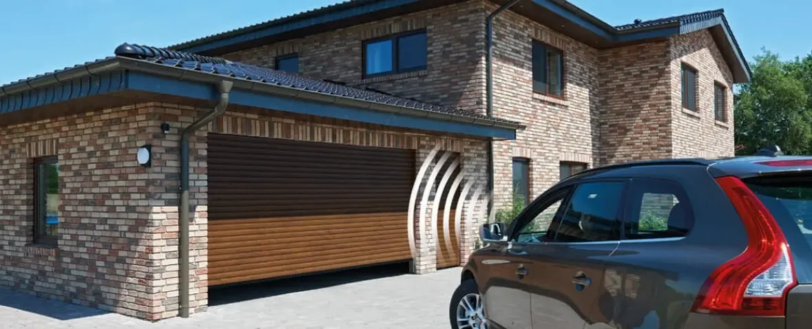 A roller garage door in a timber finish on a facing-brick house, with cars on the driveway