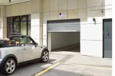 A communal garage roller door mid-opening, with a car in front of the entrance