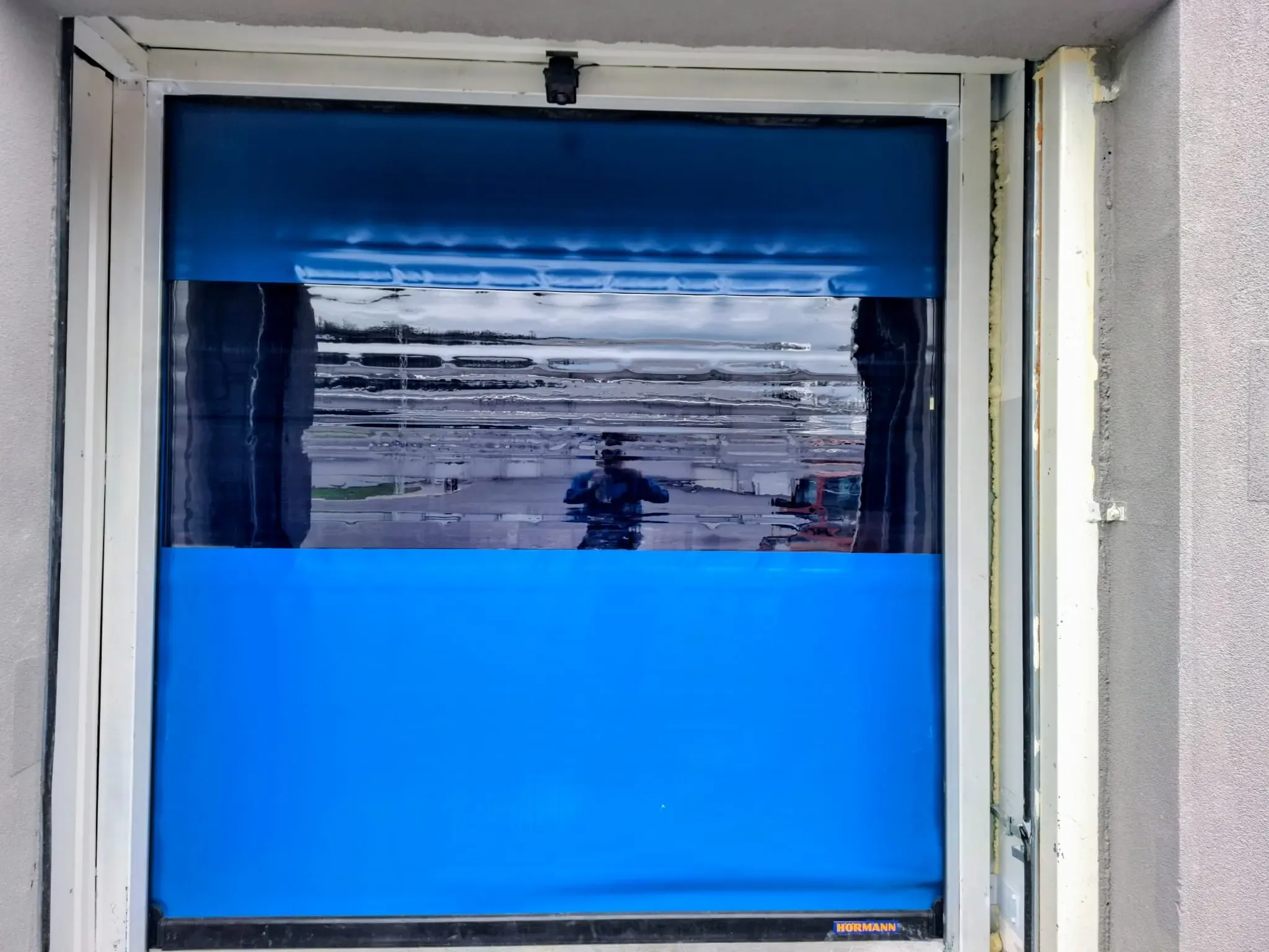 A high-speed roller door with a blue curtain and a transparent panel, mid-opening