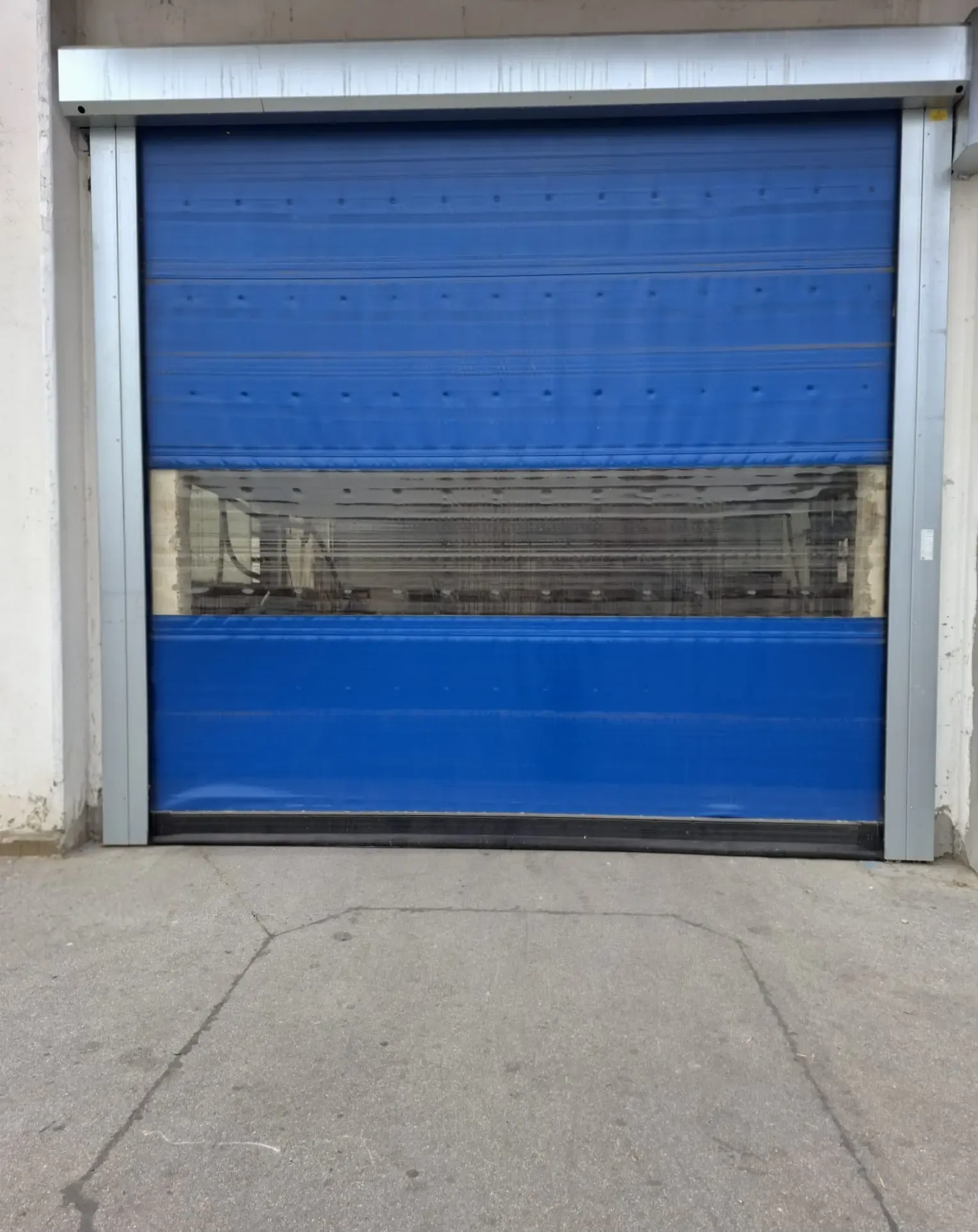 A high-speed industrial door with a blue curtain and a transparent panel, partly raised