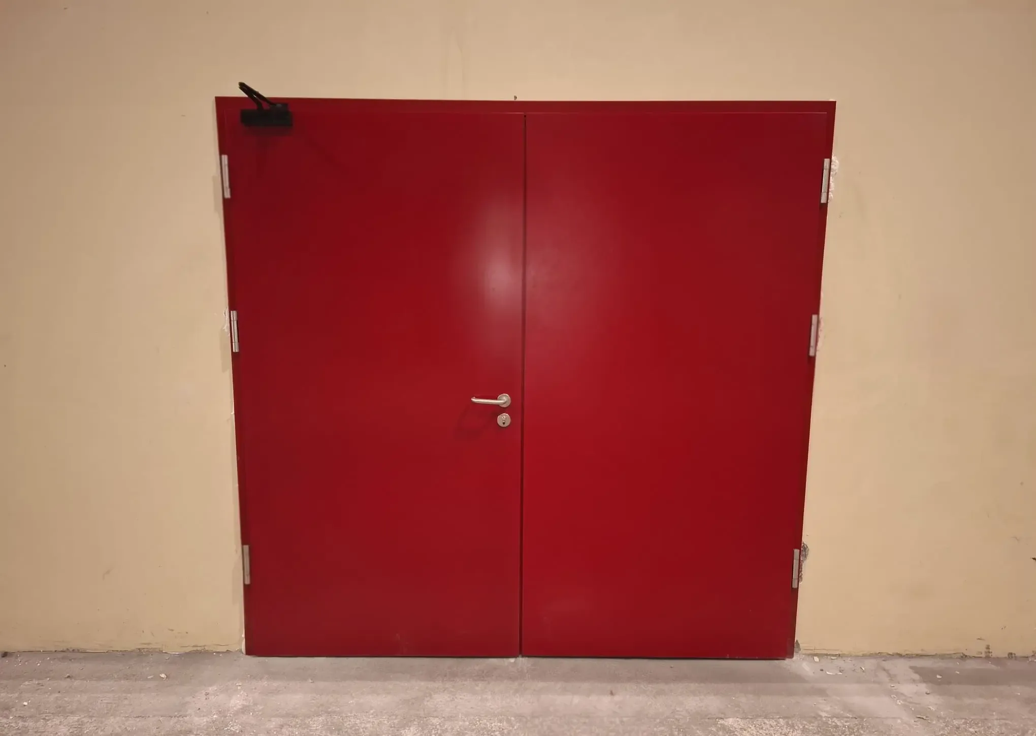 A double-leaf red steel door in the wall of an industrial building