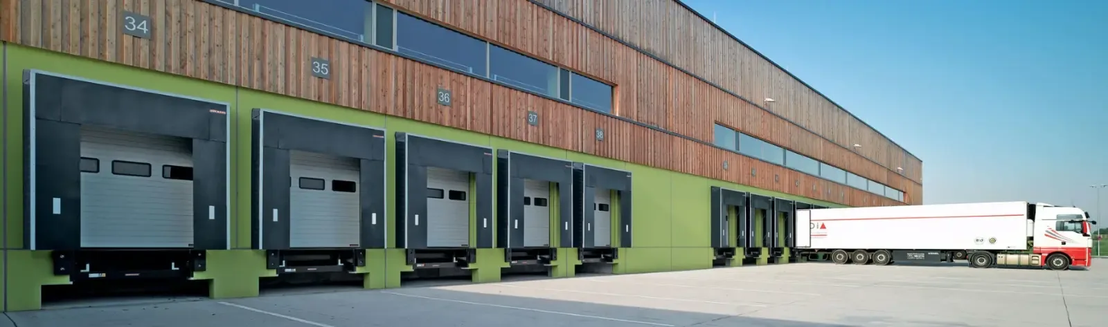 A row of loading bays with dock equipment along the façade of a logistics centre, with lorries on the yard