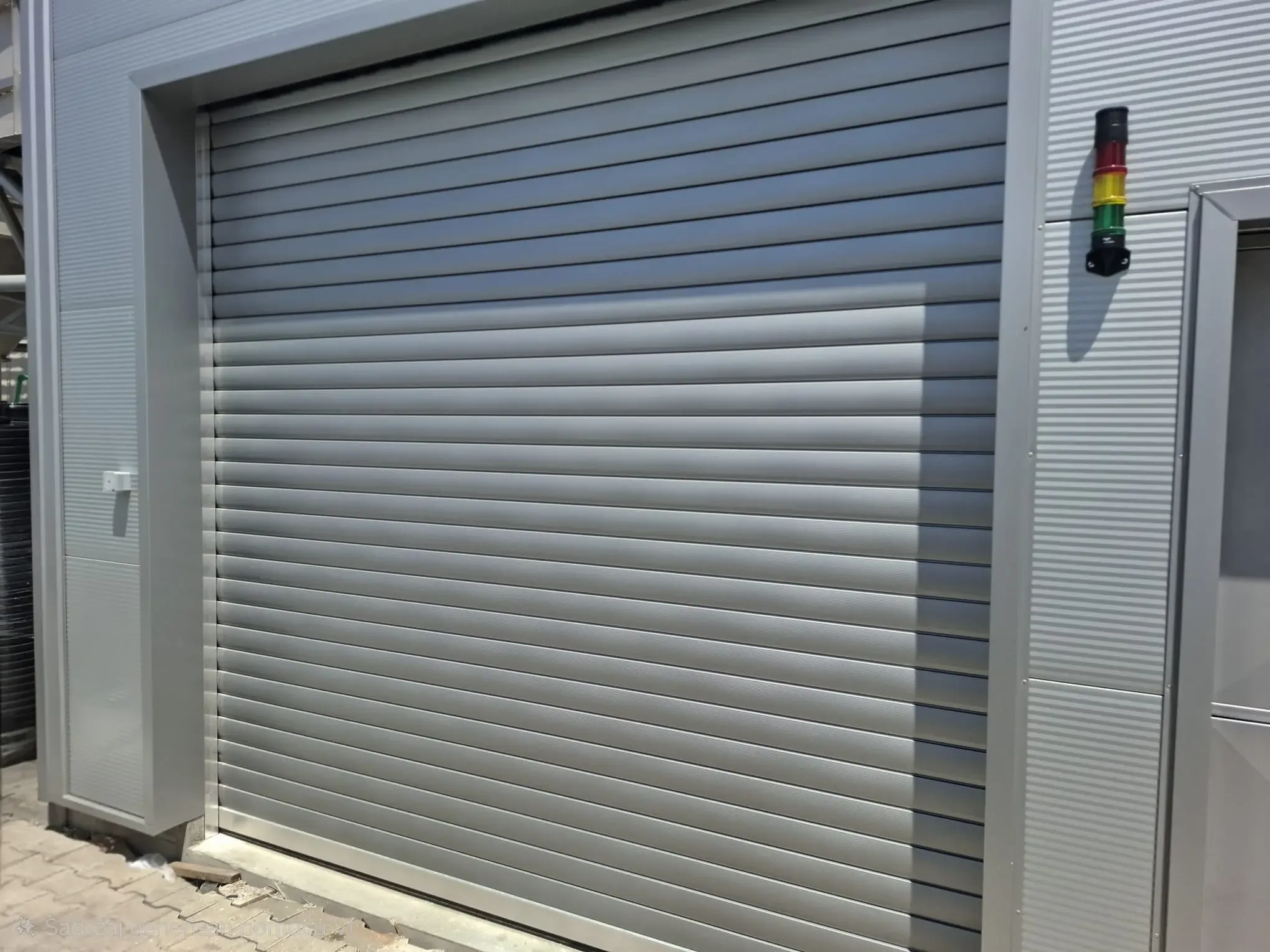 An industrial roller shutter door with steel slats and a signal column beside the opening