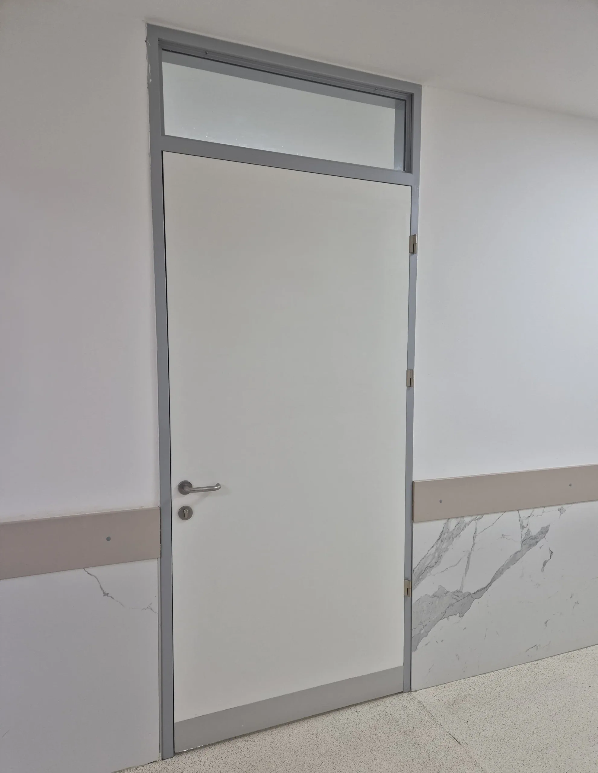 An interior door with a fanlight and a metal frame in a marble-clad corridor