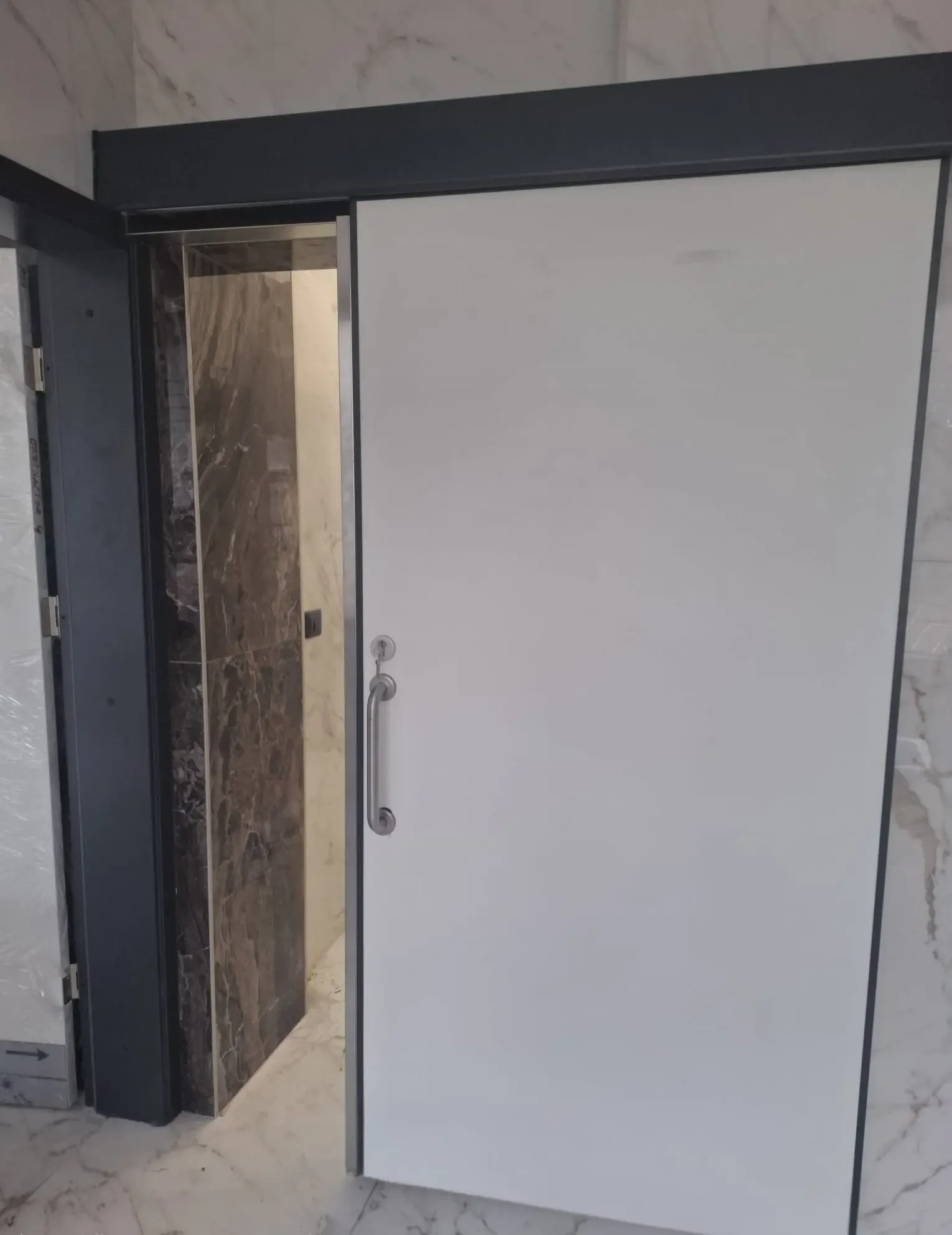 An interior sliding door with a white leaf against a dark marble-clad wall, with a vertical pull handle